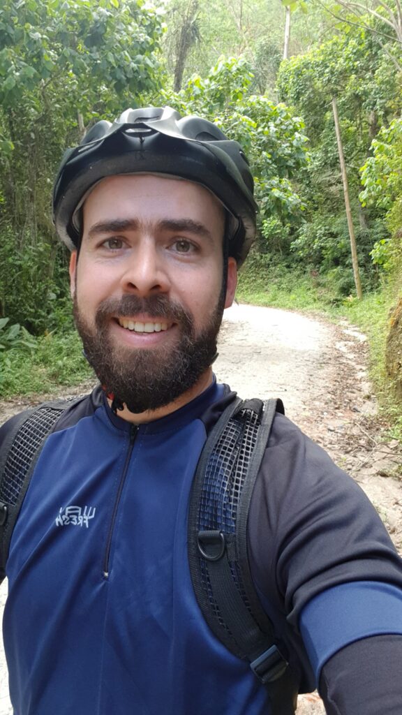 Mateus Garcia em passeio de bike em uma estrada de terra cercada por mata nativa.